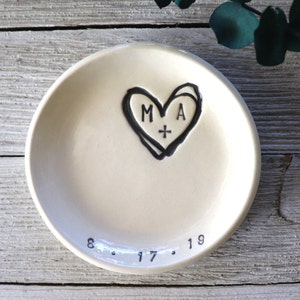 May include: White ceramic ring dish with a black hand-drawn heart design. The heart has the initials "M + A" inside and the date "8.17.19" below.