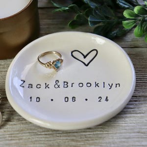Op de afbeelding: Witte keramische ringenschotel met een handgetekend hart en de tekst "Zack & Brooklyn 10.06.24".