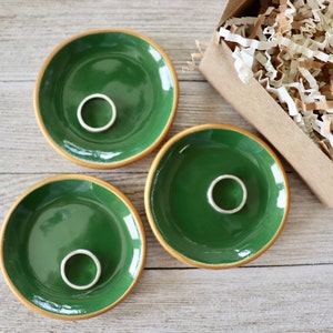 Op de afbeelding: Drie kleine groene keramische schalen met gouden randen. Elke schaal heeft een zilveren ring in het midden.