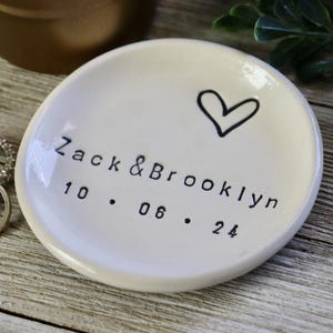 Op de afbeelding: Witte keramische ringenschotel met een handgetekend hart en de tekst "Zack & Brooklyn 10.06.24".