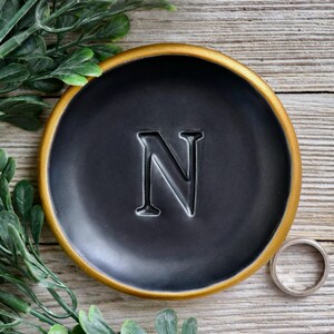 May include: A black ring dish with a gold rim and the letter "N" embossed in the center.