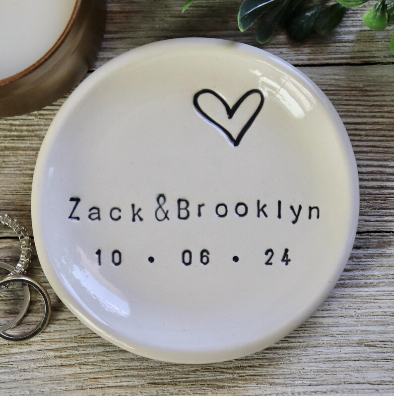 Op de afbeelding: Witte keramische ringenschotel met een handgetekend hart en de tekst "Zack & Brooklyn 10.06.24" in zwart.