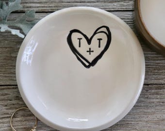 May include: White ceramic ring dish with a black hand-drawn heart and the initials "T + T" inside.