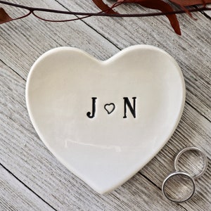 Puede incluir: Plato para anillos de cerámica blanca en forma de corazón con las iniciales "J ♥ N" en letras negras.
