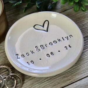 Op de afbeelding: Witte keramische ringenschotel met een handgetekend hart en de tekst "Zack & Brooklyn 10.06.24".
