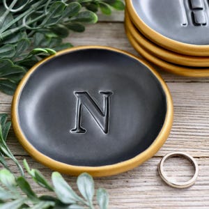 May include: Black ring dish with a gold rim and the letter "N" embossed in the center.