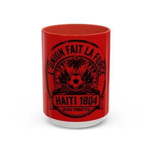 May include: A red and white ceramic mug with a black graphic design. The design includes the text "L'UNION FAIT LA FORCE", a soccer ball, and the words "HAITI 1804 NEVER FORGOTTEN".