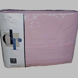 May include: A packaged king-size sheet set in a soft pink hue. The packaging includes a label with the text "KING SHEET SET" and "200 THREAD". The sheets are made by Dan River.
