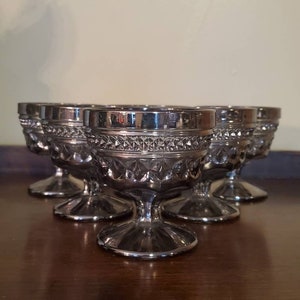 May include: Set of five silver-colored glass dessert cups with a diamond-shaped pattern. The cups have a short stem and a wide bowl.