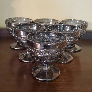 May include: Set of six silver-plated glass dessert cups with a diamond pattern. The cups have a silver rim and a clear glass base.