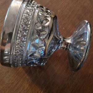 May include: A clear glass goblet with a silver rim and a cut glass design. The goblet has a wide base and a tall, slender stem.