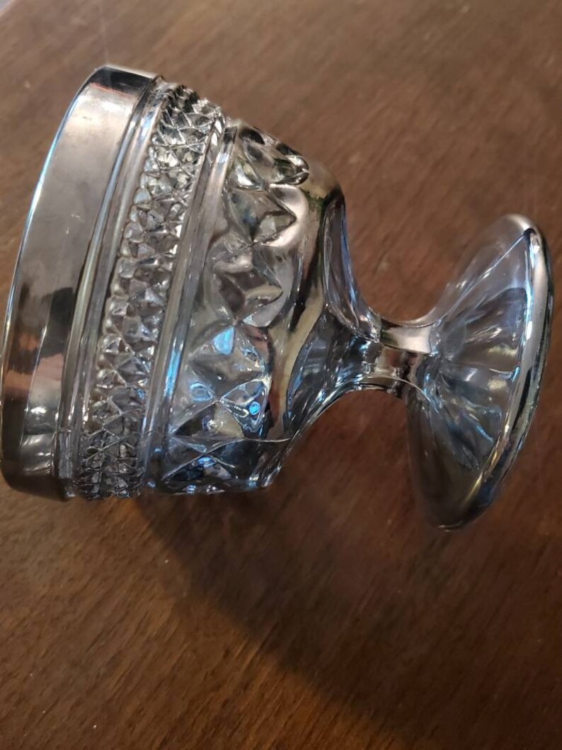 May include: A clear glass goblet with a silver rim and a cut glass design. The goblet has a wide base and a tall, slender stem.