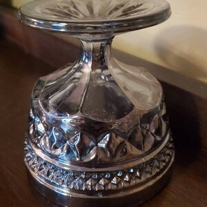 May include: A clear glass dessert bowl with a pedestal base. The bowl has a diamond pattern around the rim and a scalloped design on the sides.