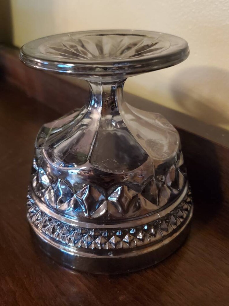 May include: A clear glass dessert bowl with a pedestal base. The bowl has a diamond pattern around the rim and a scalloped design on the sides.