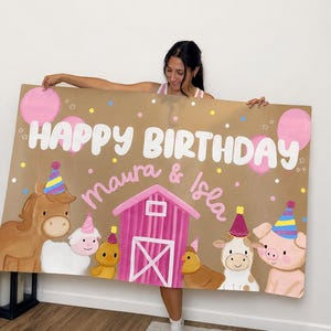 May include: A large rectangular sign with a tan background featuring the text "HAPPY BIRTHDAY" in white and "Maura & Isla" in pink. The design includes a pink barn, pink balloons, and illustrations of a horse, sheep, chick, cow, and pig wearing party hats.