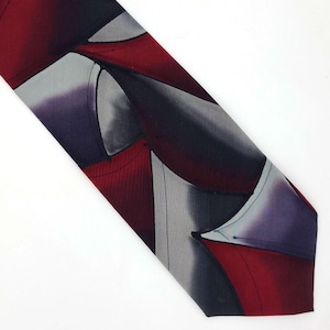 May include: A patterned necktie featuring a design with red, gray, and purple geometric shapes. The tie is angled, showcasing the repeating pattern and color variations. The tie's design is abstract and modern.