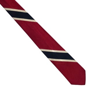 May include: A necktie featuring a diagonal striped pattern in deep red, navy blue, and off-white. The fabric has a visible ribbed texture, and the design consists of a wide red band followed by a thin off-white stripe, a navy blue stripe, and another off-white stripe, repeating across the length of the tie.