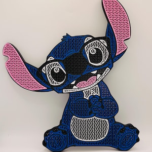 May include: A layered wall art piece depicting the character Stitch, featuring a textured blue body, large pink inner ears, black eye patches, and white accents. The design is constructed with a detailed, grid-like pattern throughout the surface.