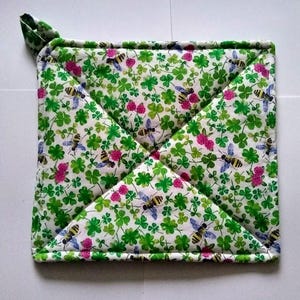 May include: A green and white quilted hot pad with a pattern of four-leaf clovers and bees. The hot pad has a hanging loop.