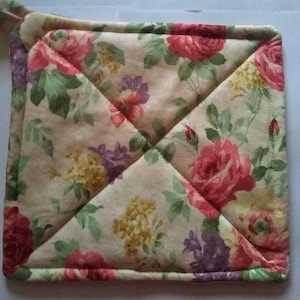 May include: Square quilted pot holder with a floral pattern. The fabric features large pink and red roses, purple and yellow flowers, and green leaves on a cream background. A loop is attached for hanging.