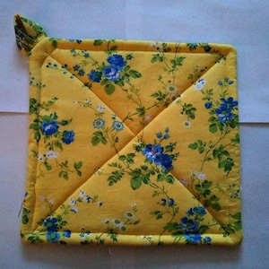 May include: Square yellow quilted pot holder with a floral pattern of blue and white flowers and green leaves. The pot holder has a loop for hanging and is edged with yellow fabric.