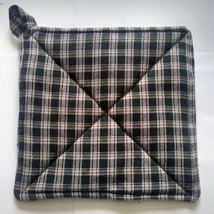 May include: A black and white plaid pot holder with a loop handle. The pot holder is made of quilted fabric and is designed to protect hands from hot surfaces.