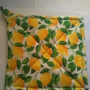 May include: A square, quilted pot holder with a vibrant lemon and leaf pattern. The design features bright yellow lemons and green leaves on a white background. The pot holder has a loop for hanging.