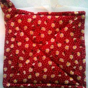 May include: A square quilted potholder featuring a vibrant red fabric base with a repeating pattern of small white daisies and tiny white dots. The item includes a fabric loop at the top corner for hanging and is stitched with a diagonal cross pattern.