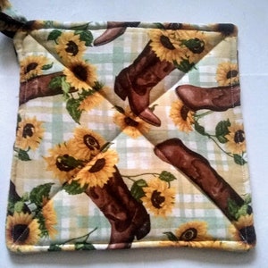 May include: Square pot holder with a repeating pattern of brown cowboy boots and yellow sunflowers on a light yellow and green plaid background. The pot holder has a loop for hanging.