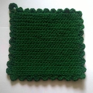 May include: A square, dark green knitted potholder with a scalloped edge and a small loop for hanging. The potholder is made of a tightly knit material, and the color is a deep, rich green.