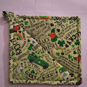 May include: A square, light yellow pot holder with a St. Patrick's Day theme. The design includes shamrocks, rainbows, leprechauns, and the text "Luck of the Irish." A green truck is also featured. The pot holder has a loop for hanging.