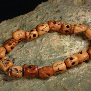 May include: A bracelet made of brown wooden beads, each carved with a skull design. The beads are strung together on a brown cord.