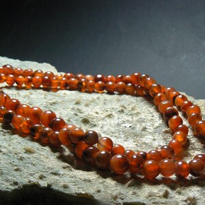 May include: A double strand necklace made of carnelian beads. The beads are a deep orange color and have a smooth, polished finish.