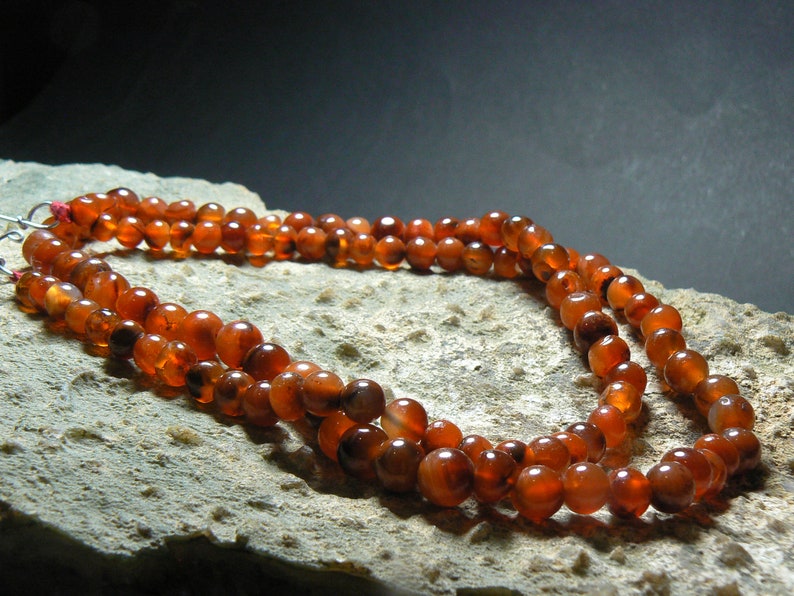 May include: A double strand necklace made of carnelian beads. The beads are a deep orange color and have a smooth, polished finish.