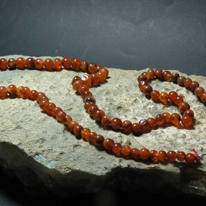 May include: A long strand of carnelian beads, with a shorter strand of carnelian beads attached to it. The beads are a deep orange-red color and are strung on a silver cord.