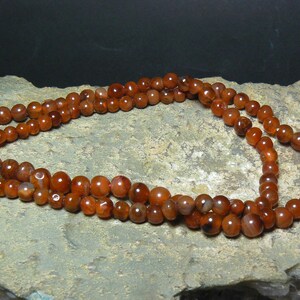 May include: A triple strand necklace made of carnelian beads. The beads are a deep orange-red color and have a natural, polished finish.