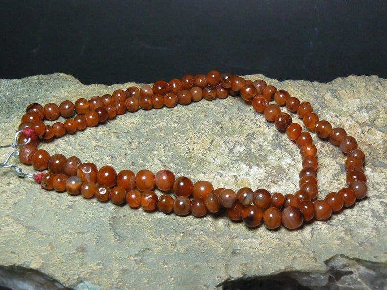 May include: A triple strand necklace made of carnelian beads. The beads are a deep orange-red color and have a natural, polished finish.