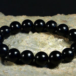 Puede incluir: Un brazalete de cuentas negras con cuentas redondas. El brazalete está hecho de piedras negras pulidas.