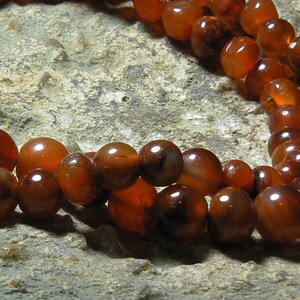May include: A strand of carnelian beads, a type of chalcedony, in shades of orange and brown. The beads are round and smooth, and they are strung on a cord.