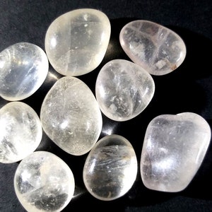 Puede incluir: Una colección de ocho piedras lisas y transparentes de cuarzo pulido. Las piedras son de varios tamaños y formas, con un tono ligeramente blanco lechoso.