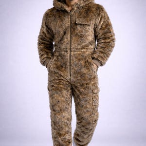 May include: Brown faux fur hooded jumpsuit with a front zipper closure, two chest pockets, and two cargo pockets on the legs. The jumpsuit is worn with white sneakers. The overall style is casual and warm.