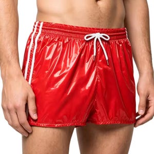 Pode incluir: Calções desportivos vermelhos brilhantes com riscas brancas nas laterais. Os calções têm um acabamento brilhante e um cordão branco. Os calções são feitos de um material leve.