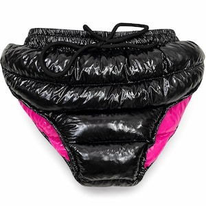 May include: Black puffer shorts with a glossy finish and a drawstring waist. The interior lining is a vibrant pink. The shorts have a unique, puffy design, offering a bold fashion statement. The garment is designed for comfort and style.