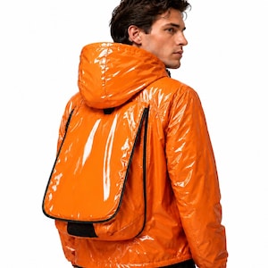Orangefarbene, glänzende Herren-Nylon-Utility-Jacke mit Kapuze und übergroßer Rückentasche