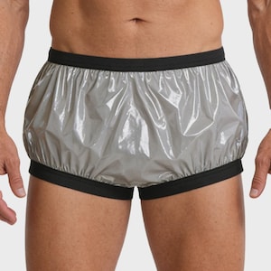 May include: Shiny, silver-grey underwear with black trim. The elastic waistband and leg openings are black. The material appears to be waterproof or water-resistant. The underwear has a loose, comfortable fit.
