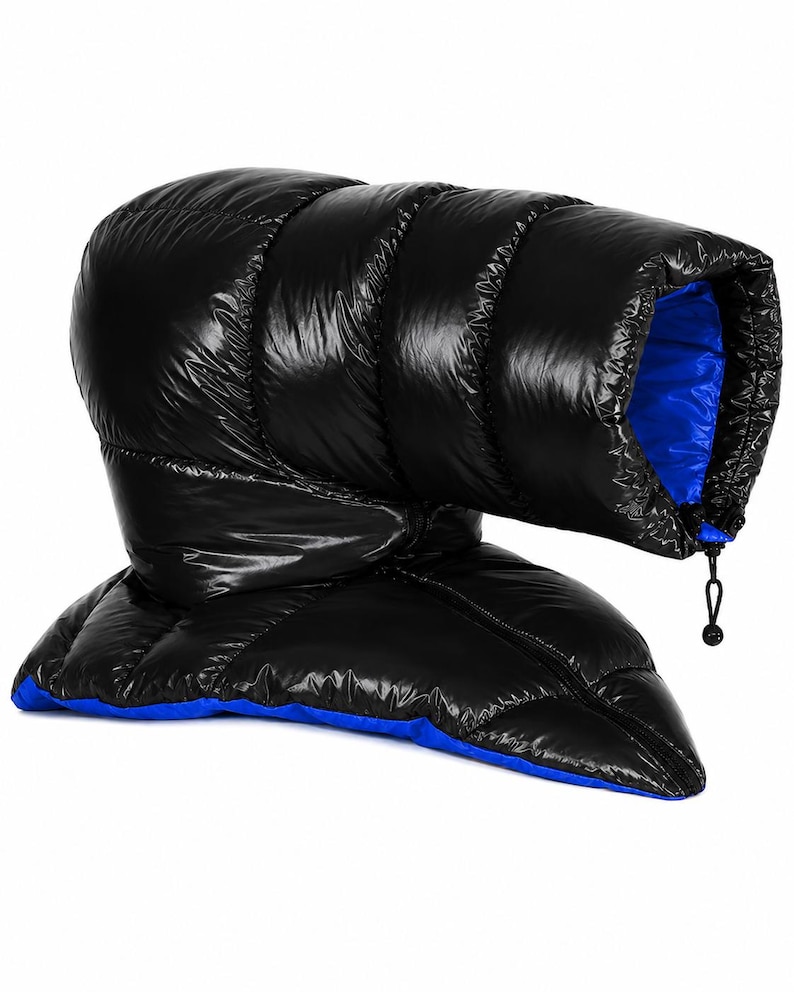K&ouml;nnte beinhalten: Ein schwarzes, gestepptes Puffer-Accessoire mit gl&auml;nzender Oberfl&auml;che und leuchtend blauem Innenfutter. Der Artikel verf&uuml;gt &uuml;ber horizontale Kammern, eine strukturierte R&ouml;hrenform und eine schwarze Kordel mit Kunststoff-Stopper.