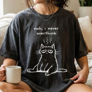 May include: A white ceramic mug with a black handle and the text "But First, Coffee" in a bold, black font. The mug is set against a blurred background, suggesting a cosy setting.
