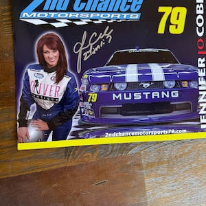 May include: A rectangular promotional card for 2nd Chance Motorsports featuring a driver in a blue and white racing suit, a purple Ford Mustang race car with the number 79, and the text Jennifer Jo Cobb. The card includes a black ink autograph.