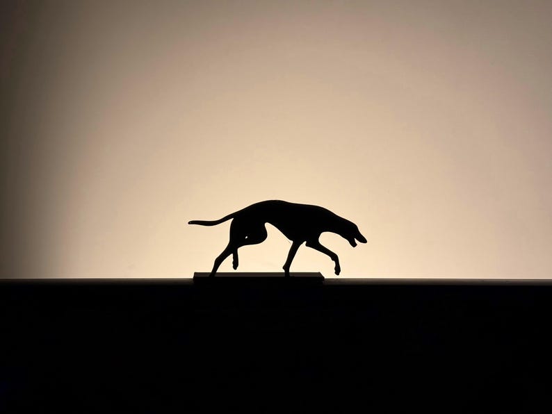以下が含まれることがあります： グラデーションの背景に、動きのある犬の黒いシルエット。 犬は長く細い体と下向きの頭で描かれており、動きと注意を暗示しています。 画像はシンプルでありながら印象的です。