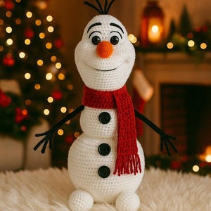 Peut inclure: Un bonhomme de neige crocheté avec une écharpe rouge, des boutons noirs et un nez en forme de carotte orange. Le bonhomme de neige a des bras en bâton noirs et se détache sur un fond flou avec un sapin de Noël et un éclairage chaleureux.